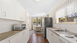 Una cocina estrecha con armarios blancos, un microondas, un refrigerador y un lavamanos.
