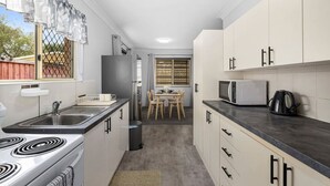Een functionele keuken met een kookplaat, spoelbak, koelkast, magnetron en een eethoek met tafel en stoelen.