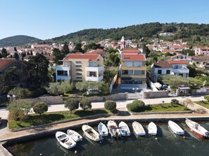 A coastal town with a marina, buildings with red-tiled roofs, and a hill in the background. - Perla Blu - Modern Seaside Escape (Preko)