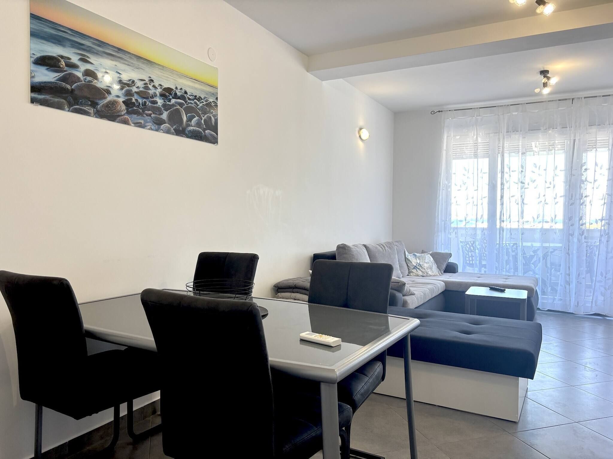A modern living room with a dining table, black chairs, a grey sofa, and a painting of a beach scene.