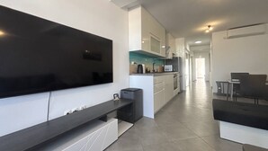 Eine moderne Küche mit Flachbildfernseher, ein Essbereich mit Tisch und Stühlen sowie ein Flur zu weiteren Zimmern.