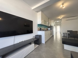 Eine moderne Küche mit Flachbildfernseher, ein Essbereich mit Tisch und Stühlen sowie ein Flur zu weiteren Zimmern.