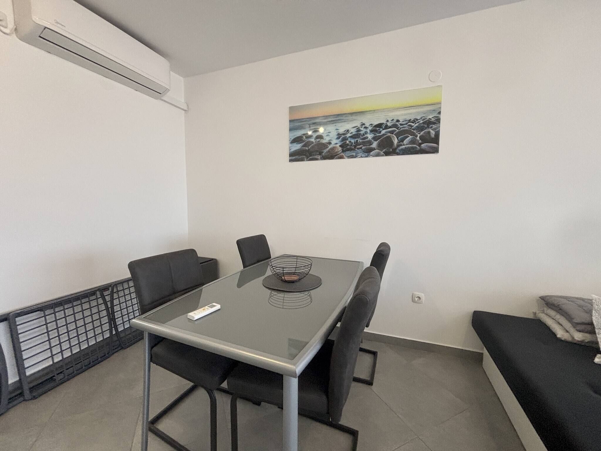 A modern dining area with a glass table, black chairs, and a painting of a rocky beach.