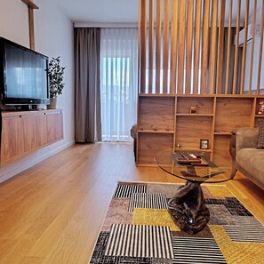 Ein modernes Wohnzimmer mit Flachbildfernseher, Holzmöbeln, einem Glastisch und einem Sofa.