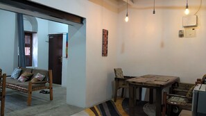 A dining area with a wooden table and chairs, a patterned rug, and a wall-mounted light fixture. - The Hub Train House Hakuna Matata (Zanzibar)