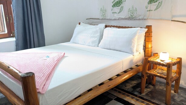 A bed with white linens, a pink blanket, and a wooden headboard.