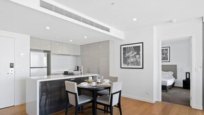 A modern kitchen with a central island, a dining area with chairs, and a bedroom visible through an open door. - Milton apartment-2BR@MT 1905 (Milton)