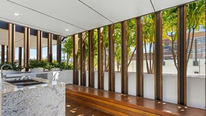 A modern outdoor seating area with a marble counter and wooden flooring, surrounded by vertical wooden slats and greenery. - Milton apartment-2BR@MT 1905 (Milton)