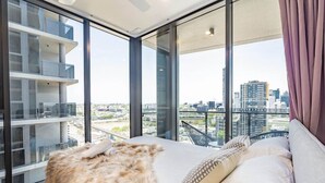Een moderne slaapkamer met een groot bed, een vacht plaid en een stadszicht door ramen van de vloer tot aan het plafond.