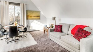 Ett modernt vardagsrum med en grå soffa, svarta stolar, ett matbord med en vas med blommor och en tavla på väggen.