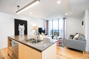Eine moderne Küche mit Kochinsel, einem Essbereich mit Tisch und Stühlen, einem grauen Sofa und einem großen Fenster mit Ausblick.