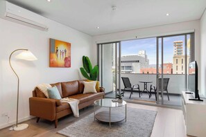 Un salon moderne avec un canapé en cuir, une table basse en verre et un balcon doté d’un espace salon extérieur.