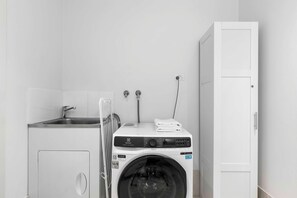 Un espace buanderie compact comprenant un lave-linge, un évier et un meuble de rangement.