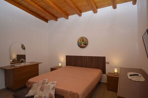 Un dormitorio con techo de madera, una cama con cabecera, una mesita de noche con lámpara, un aparador y un espejo fijado a la pared.