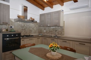 Una cocina con estufa, horno y pileta, muebles de madera y una mesa de comedor con un florero.