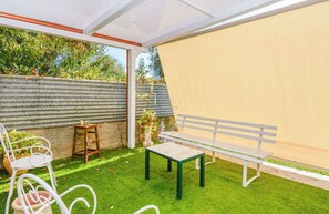 Un patio con un banco blanco, una mesita y una silla blanca.