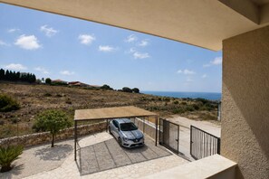 Ein Balkon mit einem darunterliegenden überdachten Parkbereich, mit Blick auf eine hügelige Landschaft und das Meer.