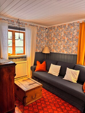 Ein Wohnzimmer mit einer Couch, einer Holzkiste und einem Fenster mit Vorhängen.