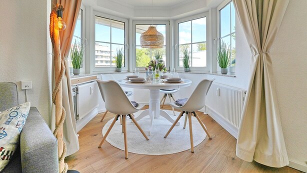 A dining area with a round table, two chairs, a hanging light fixture, and a view through large windows. - Seesternresidenz Apartment 19 - Seesternresidenz (Scharbeutz)