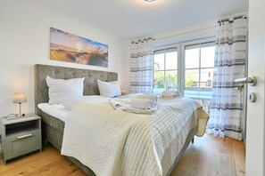 Ein Schlafzimmer mit einem Bett, Nachttischen, einem Gemälde und einem Fenster mit Vorhängen.