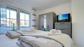 A hotel room with a bed, a TV, and a view of buildings outside. - Seesternresidenz Apartment 19 - Seesternresidenz (Scharbeutz)
