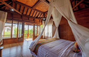 Ein Zimmer mit Holzboden, einem Bett, Vorhängen und Blick ins Freie.
