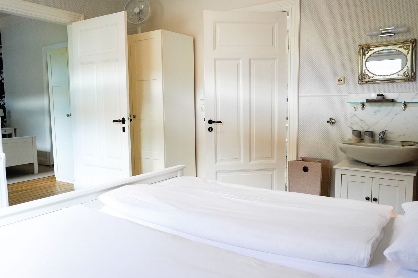 Un dormitorio con cama, armario blanco y baño con lavabo y espejo.