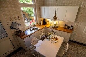 A kitchen with a window, white cabinets, a sink, a dining table with chairs, and a hanging light fixture. - Vacation apartment LOTTTALEBEN 1 - Holiday apartment "LOTTTALEBEN 1" up to 4 persons (Timmendorfer Strand)
