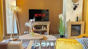 Una sala de estar acogedora con televisor, chimenea, sofá amarillo y una mesita con objetos decorativos.