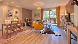 Un amplio espacio de estar con piso de madera, un sillón amarillo, una mesa de comedor y un sofá.