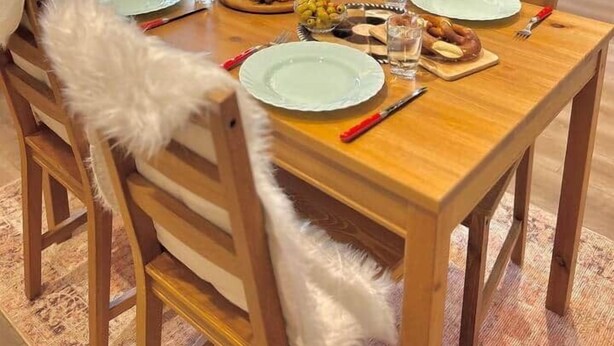 Comedor con mesa de madera dispuesta para cuatro personas, rodeado de sillas con mantas de piel blanca.