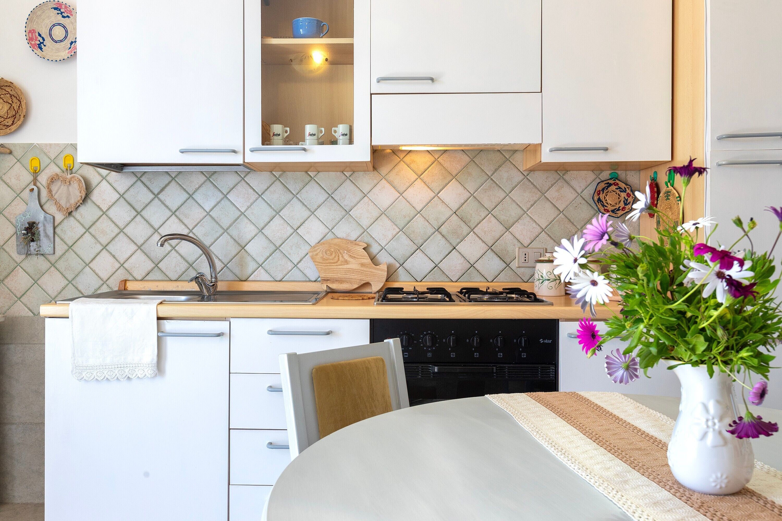 A kitchen with white cabinets, a stove, and a dining table with a vase of flowers.