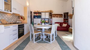 Una cocina compacta con armarios blancos, una mesa de comedor con sillas, un sofá rojo y una estantería.