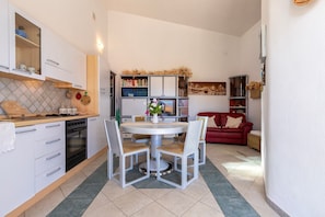 Une cuisine compacte avec des meubles blancs, une table à manger avec des chaises, un canapé rouge et une bibliothèque.
