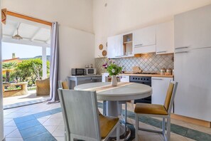 Une cuisine moderne avec des meubles blancs, une table à manger avec des chaises et une vue sur l’extérieur.