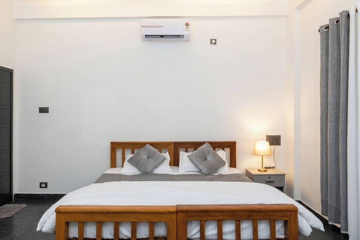 A bedroom with a double bed, a bedside table with a lamp, an air conditioning unit, and a radiator.