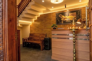 Un interior moderno con una escalera, un banco de madera, un escritorio con lámpara y un cuadro en la pared.