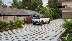 Um SUV branco estacionado em um caminho de azulejos, com uma casa e vegetação exuberante ao fundo.