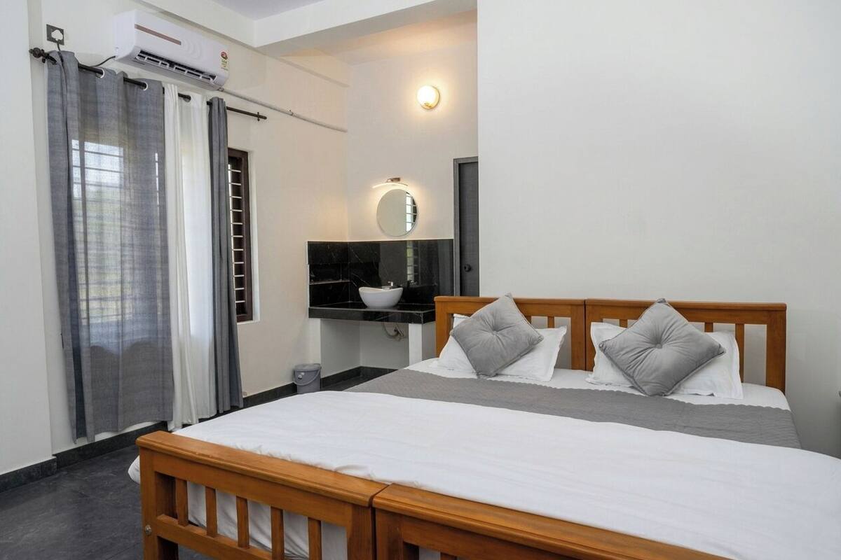 A bedroom with a bed, a bedside table, a mirror, and a window with curtains.