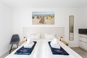 A hotel room with a bed, a chair, a desk, a mirror, and a beach scene painting. - MEERholung Vacation Rental 2.4 for up to 4 people, just 400 m from the sea - House (Cuxhaven)