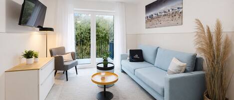 A modern living room with a sofa, a coffee table, a TV, and a balcony with plants.