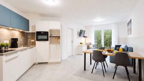 A modern kitchen with a built-in oven, a coffee machine, and a dining area with a table and chairs. - MEERholung House, Vacation Rental 2.5 - About 400 m from the beach, for up to 4 guests - House (Cuxhaven)