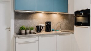 Ett modernt kök med vita skåp, ett blått överskåp, en svart kaffebryggare, en vattenkokare och en inbyggd ugn.