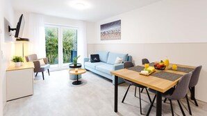 A modern living space with a dining area, a sofa, and a TV mounted on the wall. - MEERholung House, Vacation Rental 2.5 - About 400 m from the beach, for up to 4 guests - House (Cuxhaven)
