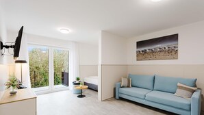 Ein modernes Wohnzimmer mit einem hellblauen Sofa, einem kleinen runden Tisch und einem an der Wand befestigten Fernseher.