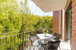 Un balcon avec une table et des chaises, un vase rempli de fleurs et une vue sur les arbres.