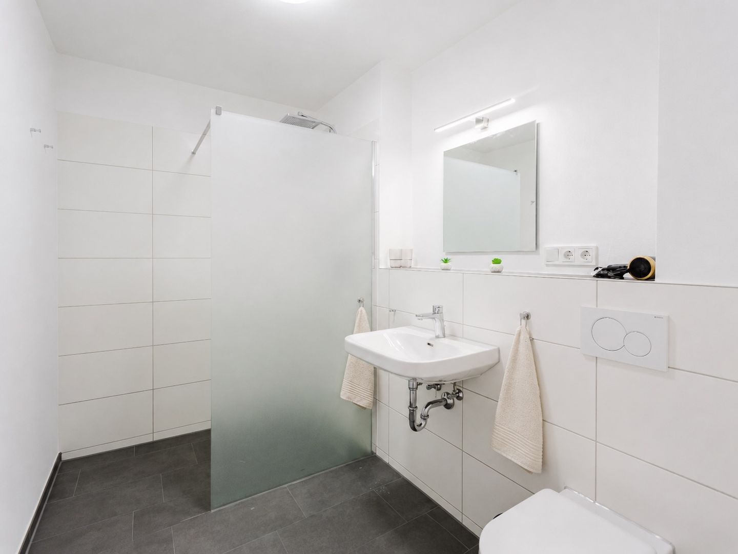 Een moderne badkamer met een douche, wastafel en toilet.
