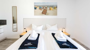 A hotel room with a bed, two bedside tables, a mirror, and a beach-themed painting on the wall. - MEERholung Vacation Rental 2.3: Close to the Beach with a Balcony for Up to 4 Guests - MEERholung House (Cuxhaven)