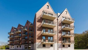 Un edificio residencial de varios pisos con balcones, fachada de ladrillo y cielo despejado.