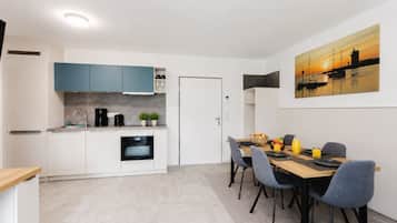 Eine moderne Küche mit weißen und blauen Schränken, ein Essbereich mit Tisch für zwei Personen und ein Sonnenuntergangsbild an der Wand.